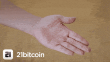 a person is holding a gold coin in their hand with the 21bitcoin logo in the background