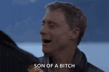 a man is talking to another man with his mouth open and says son of a bitch .