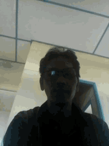 a man wearing glasses and a black shirt looks down at the camera