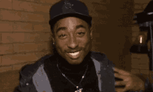a man wearing a hat and a jacket is smiling in front of a brick wall .