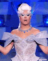 a drag queen is wearing a silver dress and a necklace and earrings