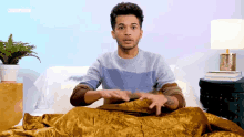 a man in a blue sweater is sitting on a bed under a blanket with the word cosmopolitan on the bottom right