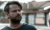 a man with a beard wearing a black shirt is standing in front of a building .