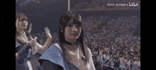 a girl in a blue dress is standing in front of a crowd with the words mygo ave mujica on the bottom right