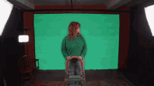 a woman in a green sweater is sitting on a ladder in front of a green screen