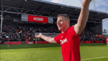 a man in a red shirt is standing on a soccer field with his arms in the air