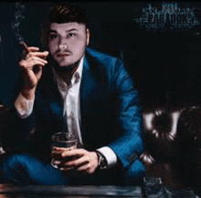 a man in a blue suit is smoking a cigarette and drinking a glass of whiskey .