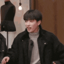 a young man in a black jacket is standing in front of a mannequin and making a funny face .