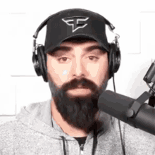 a man with a beard is wearing headphones and a hat and talking into a microphone .