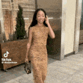 a woman in a yellow dress is walking down a sidewalk while talking on a cell phone .