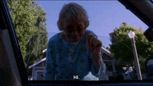 an elderly woman wearing glasses and a nose ring says hi in a car window