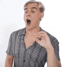 a man in a black and white shirt is yawning with his mouth wide open .