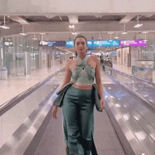 a woman in a green top and blue pants is walking down an escalator at an airport