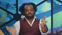 a man in a maroon vest and white shirt is making a gesture with his hands