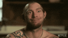 a shirtless man with tattoos on his chest is smiling in a netflix video