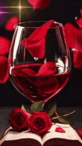 a glass of red wine sits on an open book with two red roses