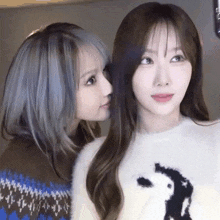 two young women are standing next to each other and one is whispering into the other 's ear .