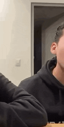 a man in a black hoodie is sitting at a table and talking to someone .