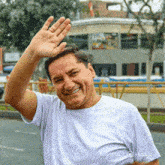 a man in a white shirt is smiling and waving at the camera