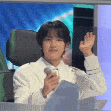 a young man in a white suit is sitting in front of a microphone and waving .