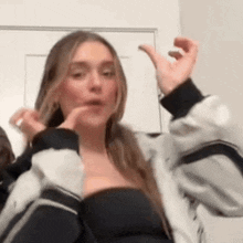 a woman in a black top and a gray jacket is making a funny face with her hands in the air .