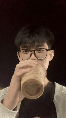 a young man wearing glasses is drinking a cup of coffee