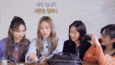 a group of girls are sitting around a table and one of them is holding a camera with korean writing on it