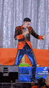 a man in a sequined jacket is singing into a microphone while standing on a stage .