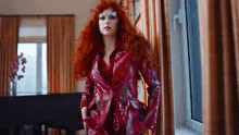 a woman with red hair is standing in front of a window in a room .