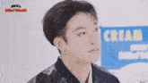 a close up of a young man standing in front of a sign that says cream .
