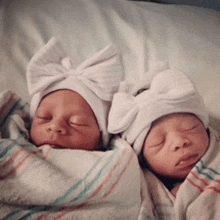 two newborn babies wearing white hats with bows