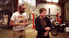 a man wearing a t-shirt with a picture of a car on it stands next to another man in a garage