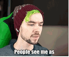 a man with green hair and a beard is wearing a burgundy beanie and says people see me as