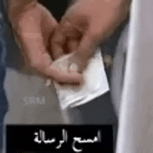a close up of a person 's hands holding a piece of paper with arabic writing on it .