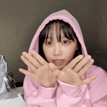 a girl in a pink hoodie is making a face with her hands
