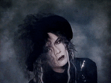 a woman wearing a black hat and a black jacket is looking at the camera