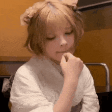 a little girl with blonde hair is sitting in a chair with her hands on her face .