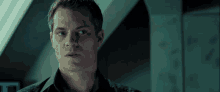 a man in a black shirt looks at the camera with a serious look on his face