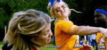 two cheerleaders are fighting on a field and one of them is wearing a yellow jersey .