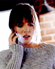 a woman in a grey sweater is talking on her cell phone