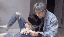 a man in a denim jacket is holding another man 's leg