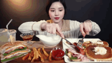 a woman sits at a table with a plate of food including a sandwich and pancakes