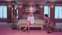 a woman is sitting on a bench in a room with two men kneeling around her .
