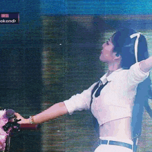 a woman in a white crop top and tie is singing into a microphone on stage .