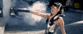 a woman is holding a gun with smoke coming out of it .