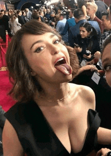 a woman is sticking her tongue out in front of a crowd of people on a red carpet .