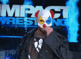 a man in a clown mask stands in front of an impact wrestling sign