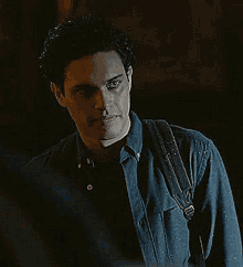 a man in a blue shirt is standing in the dark with a backpack on his back .