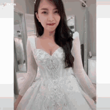 a woman in a white wedding dress is standing in front of a mirror in a room .