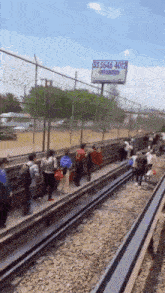 a group of people are walking on train tracks in front of a billboard for 5564644012